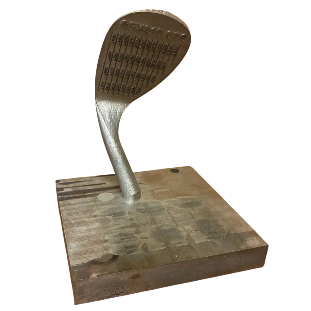 Golf wedge head printed upright on its build plate, with engraved face grooves